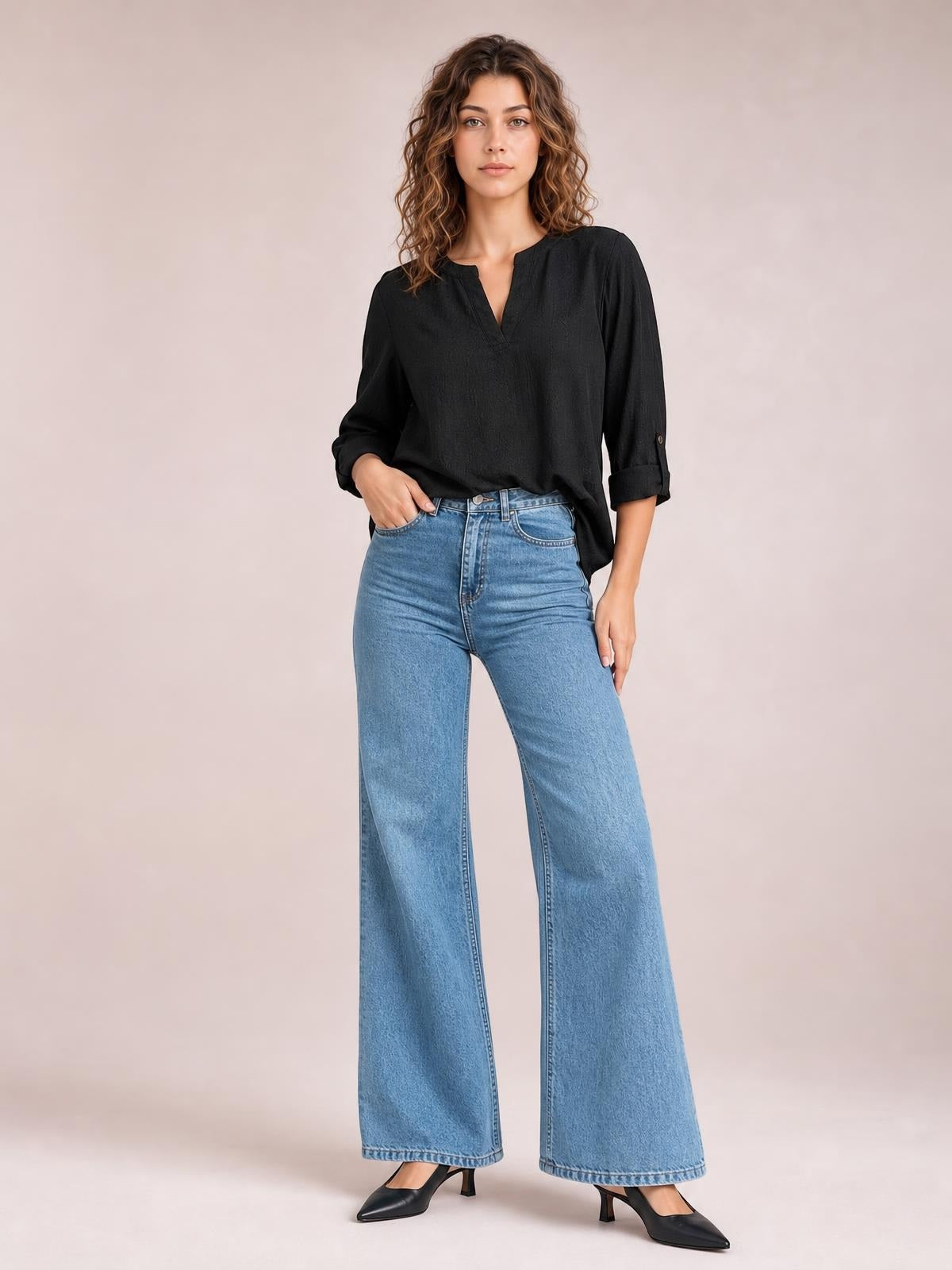 Model poses with one hand in the pocket, wearing light blue high-waisted bootcut jeans with a wide-leg silhouette, belt loops, and front pockets.