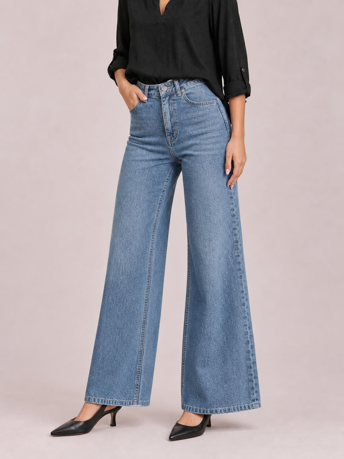 Model poses with one hand in the pocket of light blue high-waisted bootcut jeans, featuring a fitted waist, front pockets, and wide flared legs.