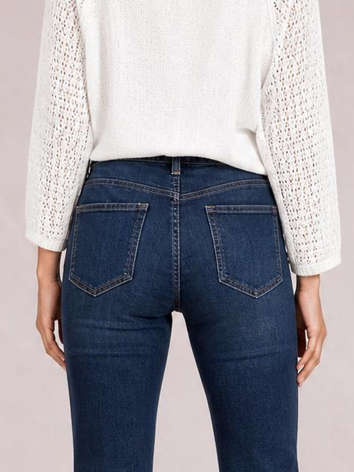 Back view of a model wearing dark blue high-waisted bootcut jeans with contrast stitching, belt loops, and two large patch pockets, standing with hands at her sides.