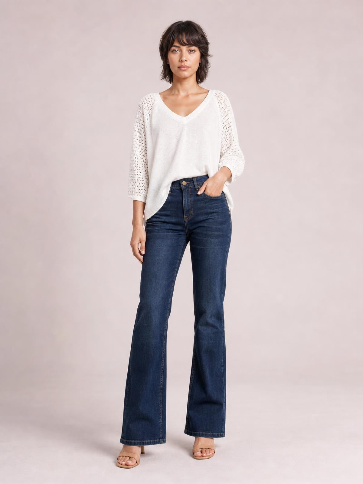 A model poses in dark blue high-waisted bootcut jeans with a button closure, front pockets, fitted hips and thighs, and gently flared hems.