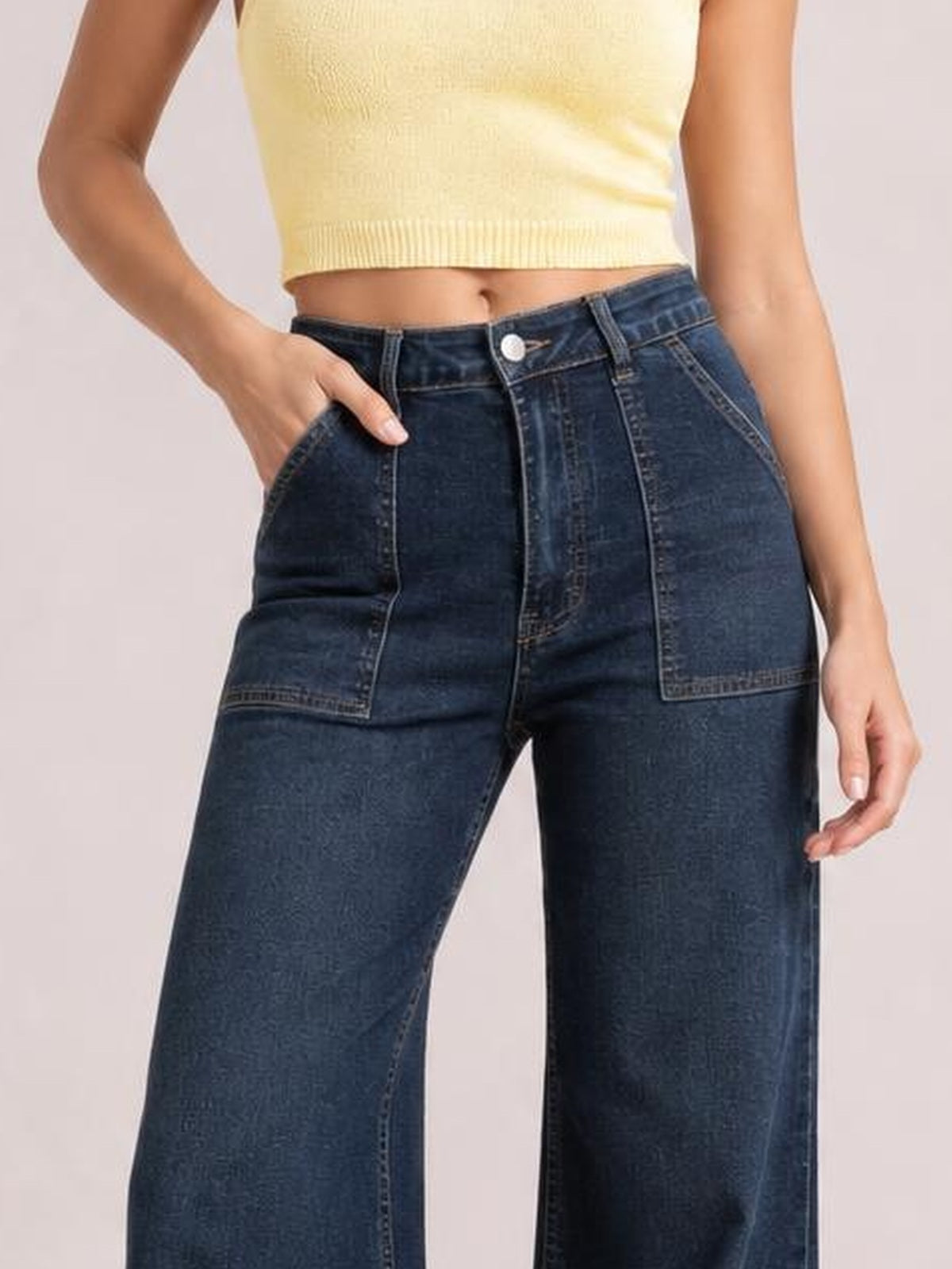 Model wearing dark blue high-waisted flare leg jeans with a button closure, front patch pockets, belt loops, and wide legs.