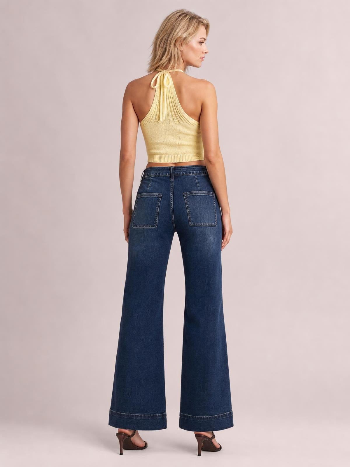 Model shown from the back wearing dark-wash high-waisted flare leg jeans with a buttoned waistband, rear patch pockets, wide hems, and a full-length silhouette.