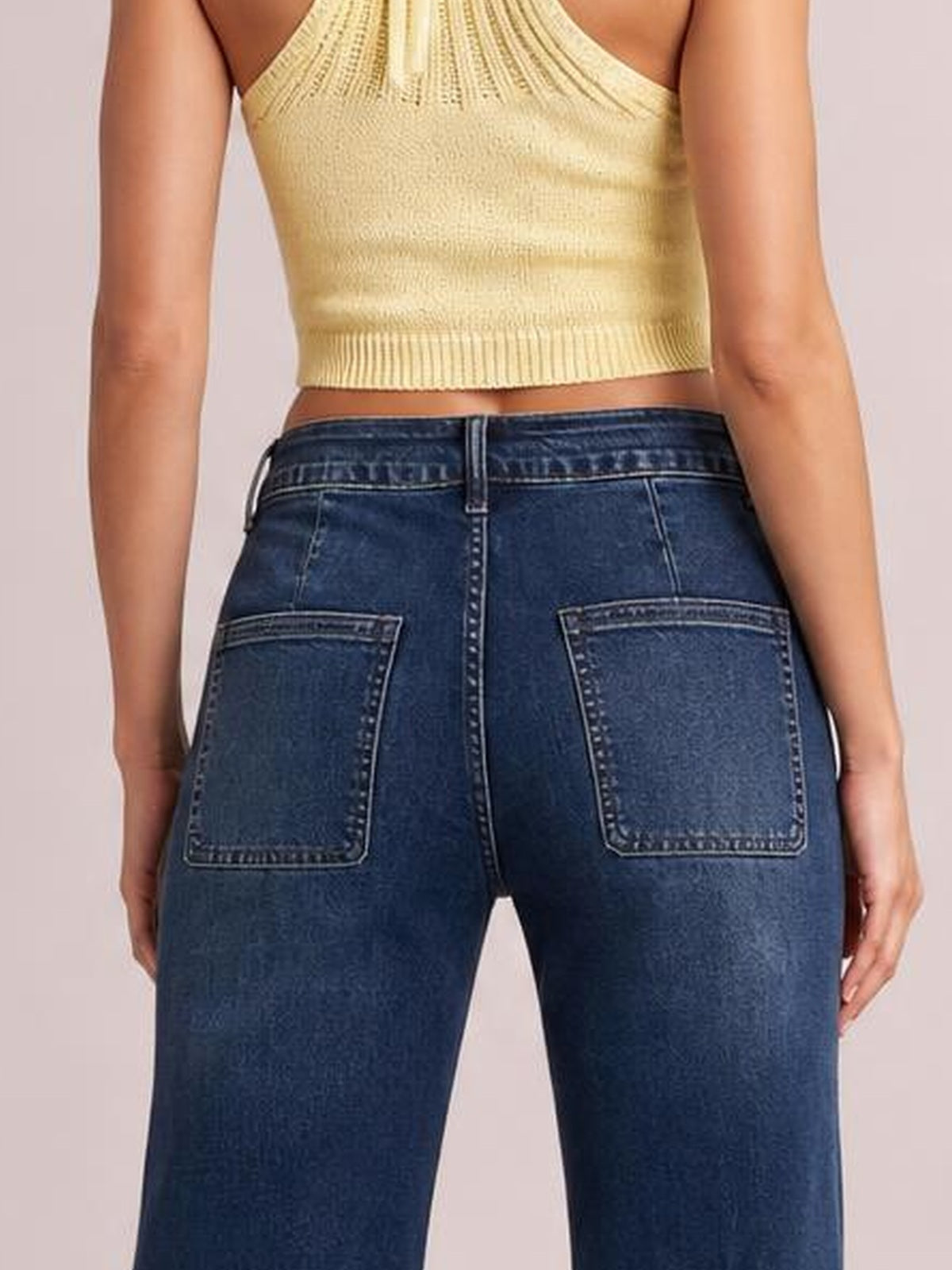 Model shown from behind wearing dark blue high-waisted flare leg jeans with belt loops, contrast stitching, and two large back patch pockets.