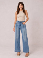 Model poses in light blue high-waisted flare leg jeans with front pockets, button closure, and visible vertical seam detailing.
