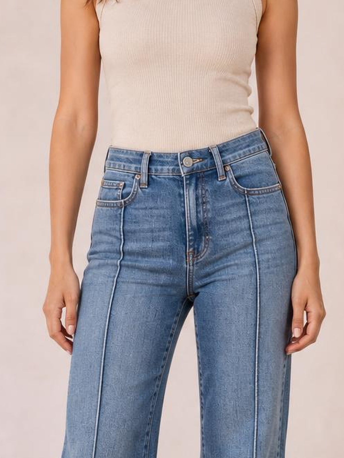 Model stands wearing light blue high-waisted flare leg jeans with a button fly, belt loops, front pockets, and contrasting vertical seam details.