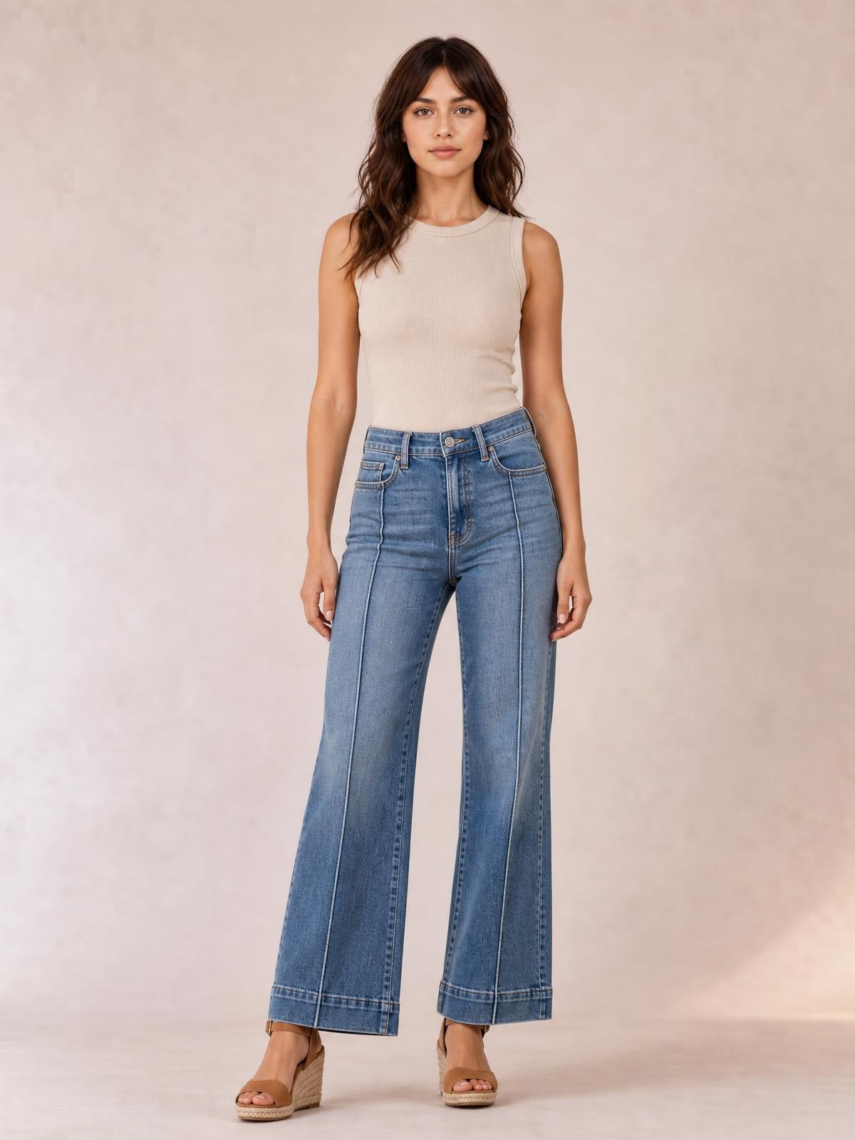 Model stands facing forward in high-waisted blue flare leg jeans with front pockets, button closure, contrast seams, and a wide-leg silhouette.