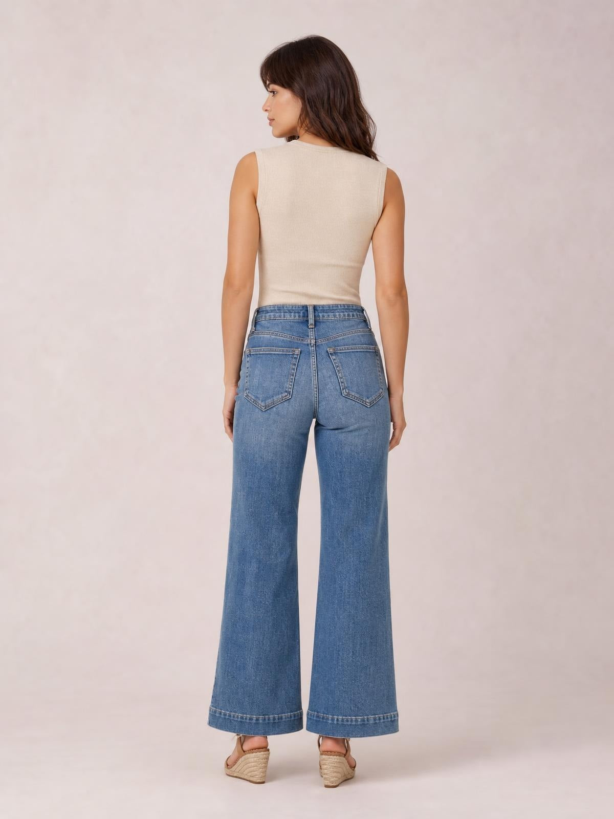 Model shown from the back wearing light blue high-waisted flare leg jeans with wide hems, belt loops, buttoned waist, and two patch back pockets.