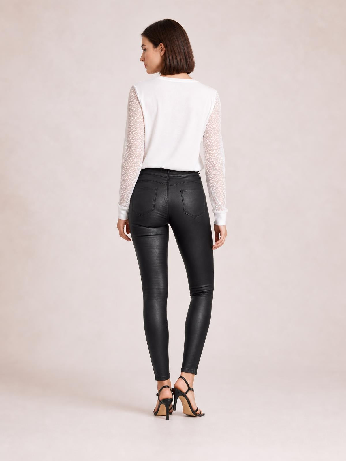 A model poses from behind in black high-waisted faux leather skinny pants with a sleek fitted silhouette, waistband, stitched seams, and two back pockets.