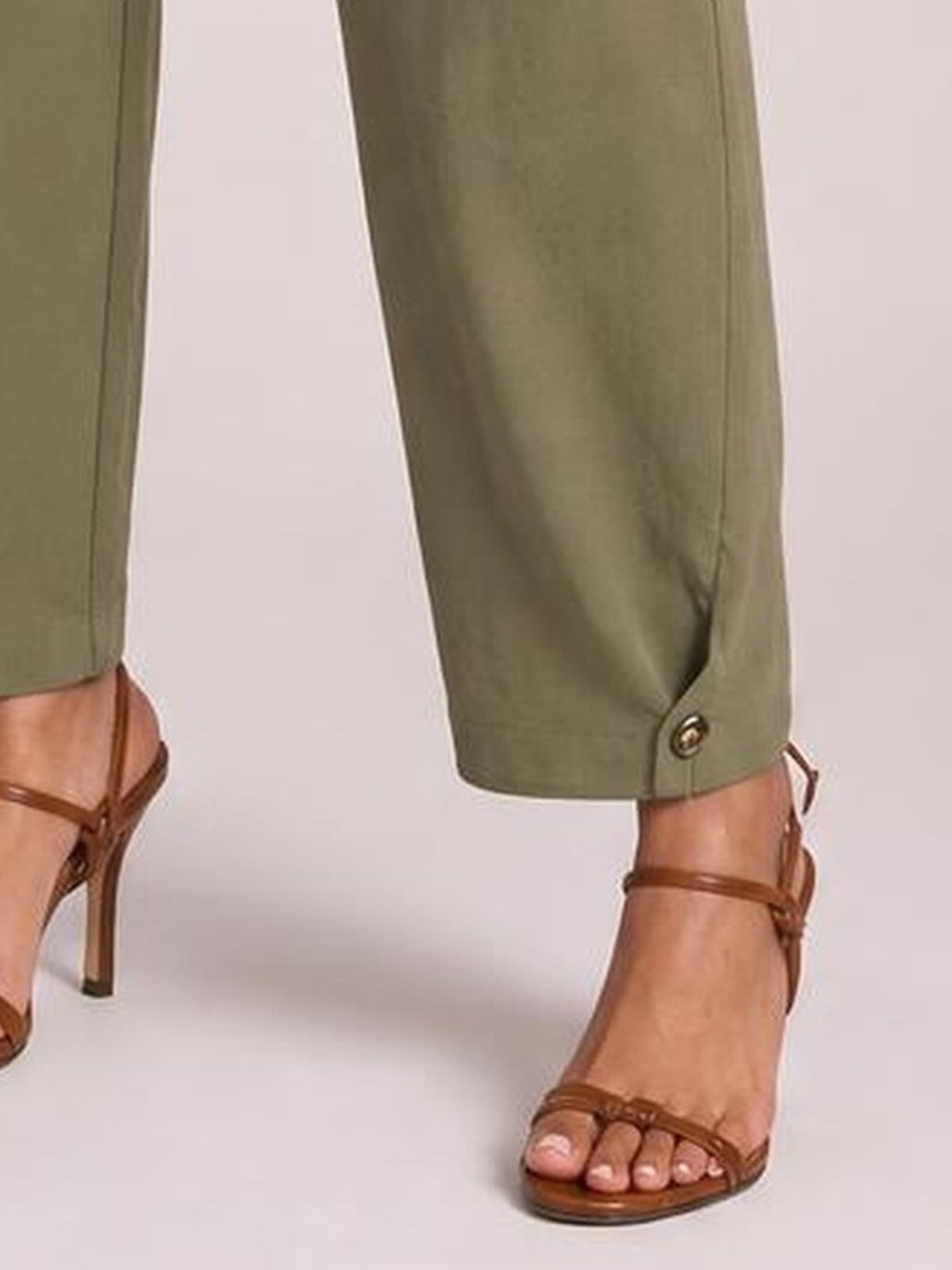 A model stands in olive-green cropped pants with straight legs, button-tab cuffs, and a polished ankle-length silhouette.