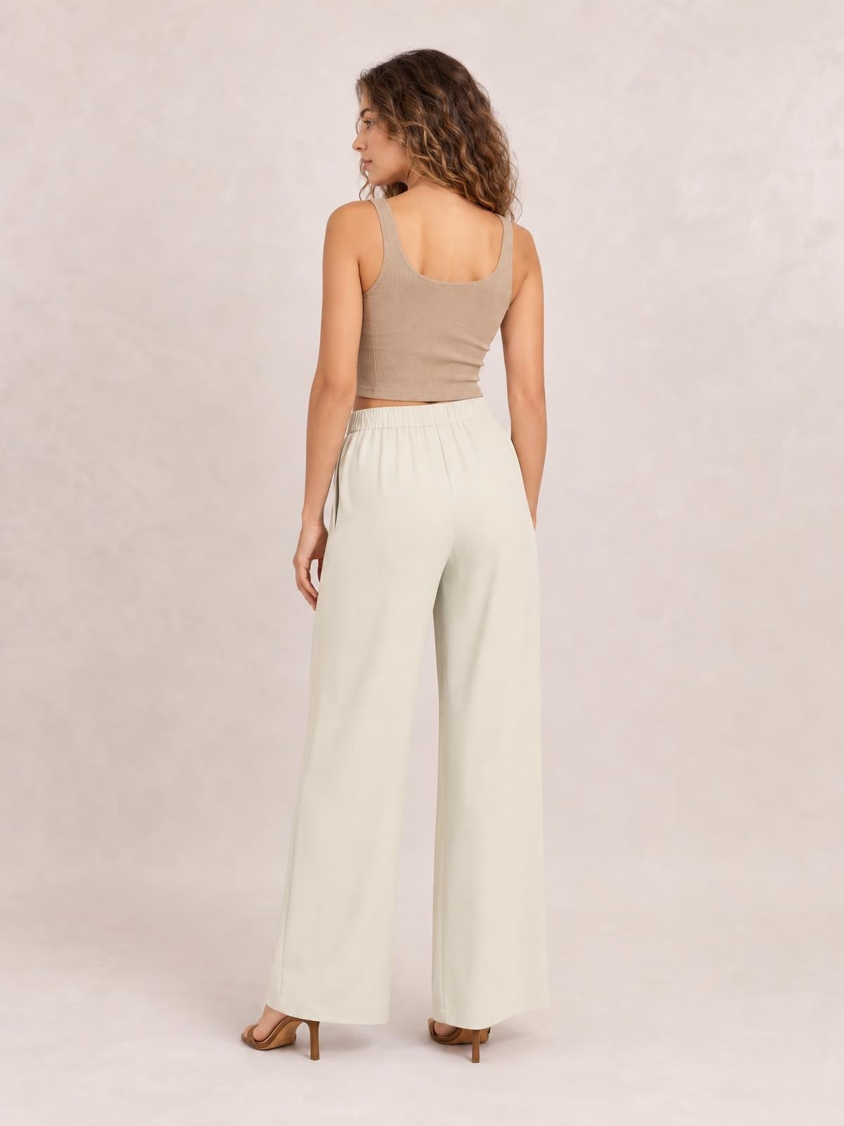 A model poses turned away in cream high-waisted pleated wide-leg pants with a relaxed silhouette and full-length legs.