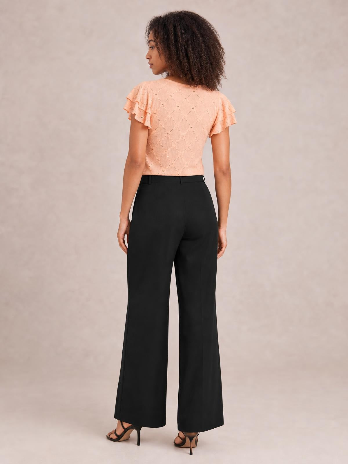 A model shown from behind wears black high-waisted wide-leg pants with a fitted waistband and full-length, flowing silhouette.