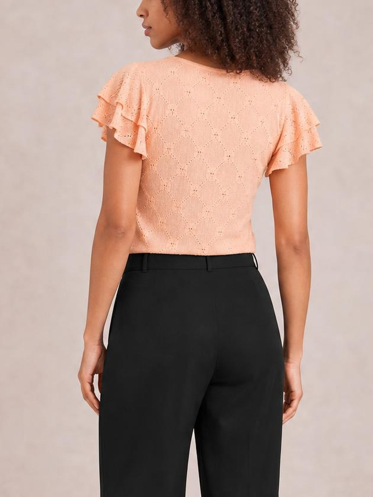 A model stands with her back to the camera wearing black high-waisted wide-leg pants with a structured waistband and visible belt loops.