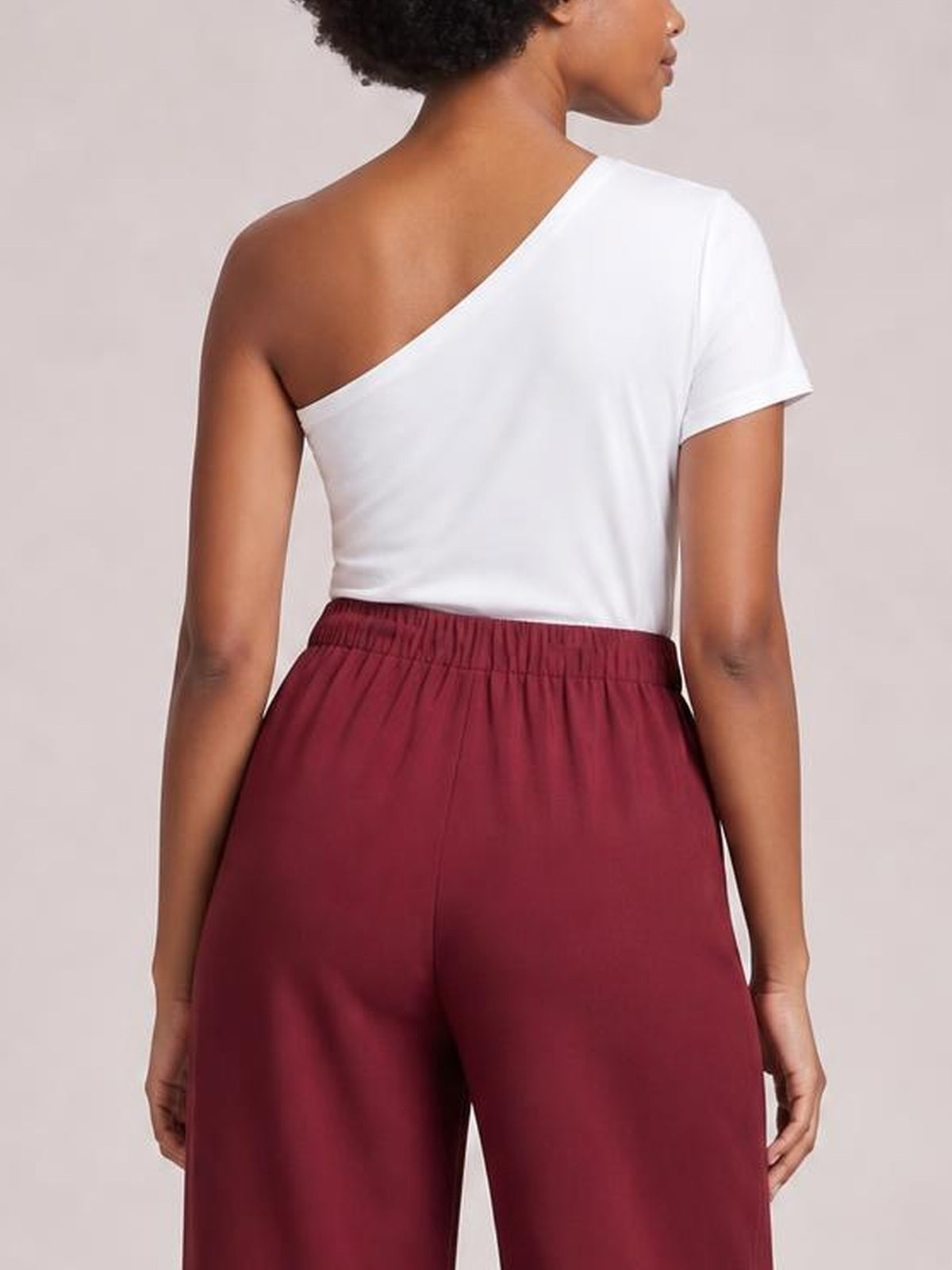 Model shown from behind wearing burgundy high-waisted pleated wide-leg pants with a gathered waistband and relaxed, flowing silhouette.