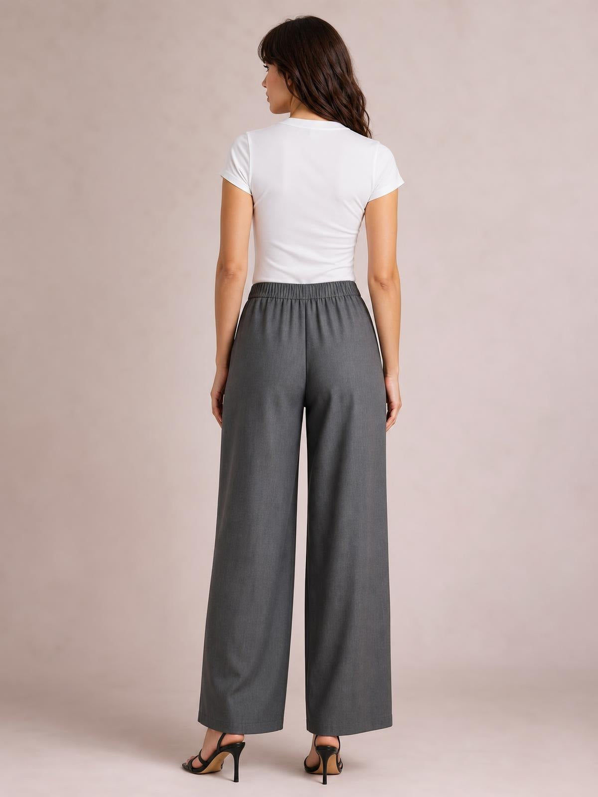 A model stands with her back to the camera wearing charcoal gray high-waisted wide-leg pants with a smooth waistband and flowing silhouette.