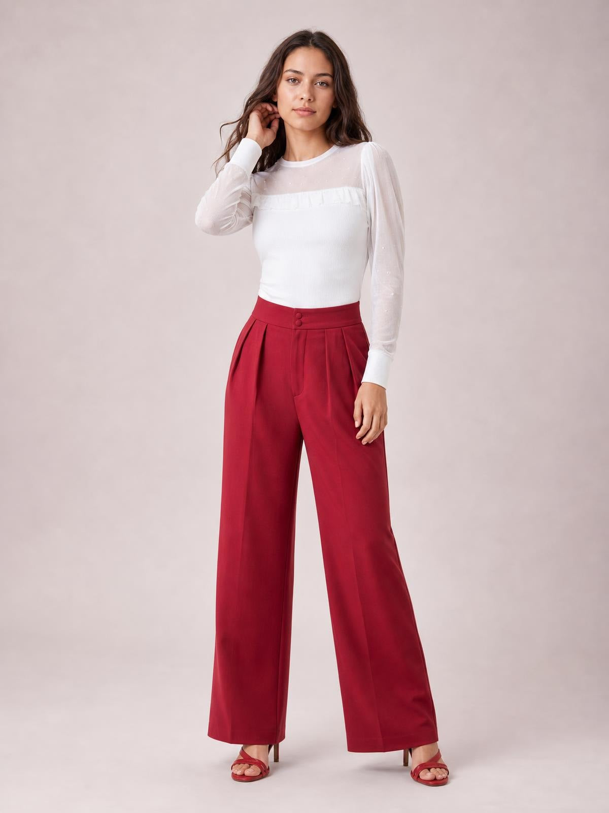 A model poses in red high-waisted pleated wide-leg pants with front buttons, side pockets, and a flowing full-length silhouette.
