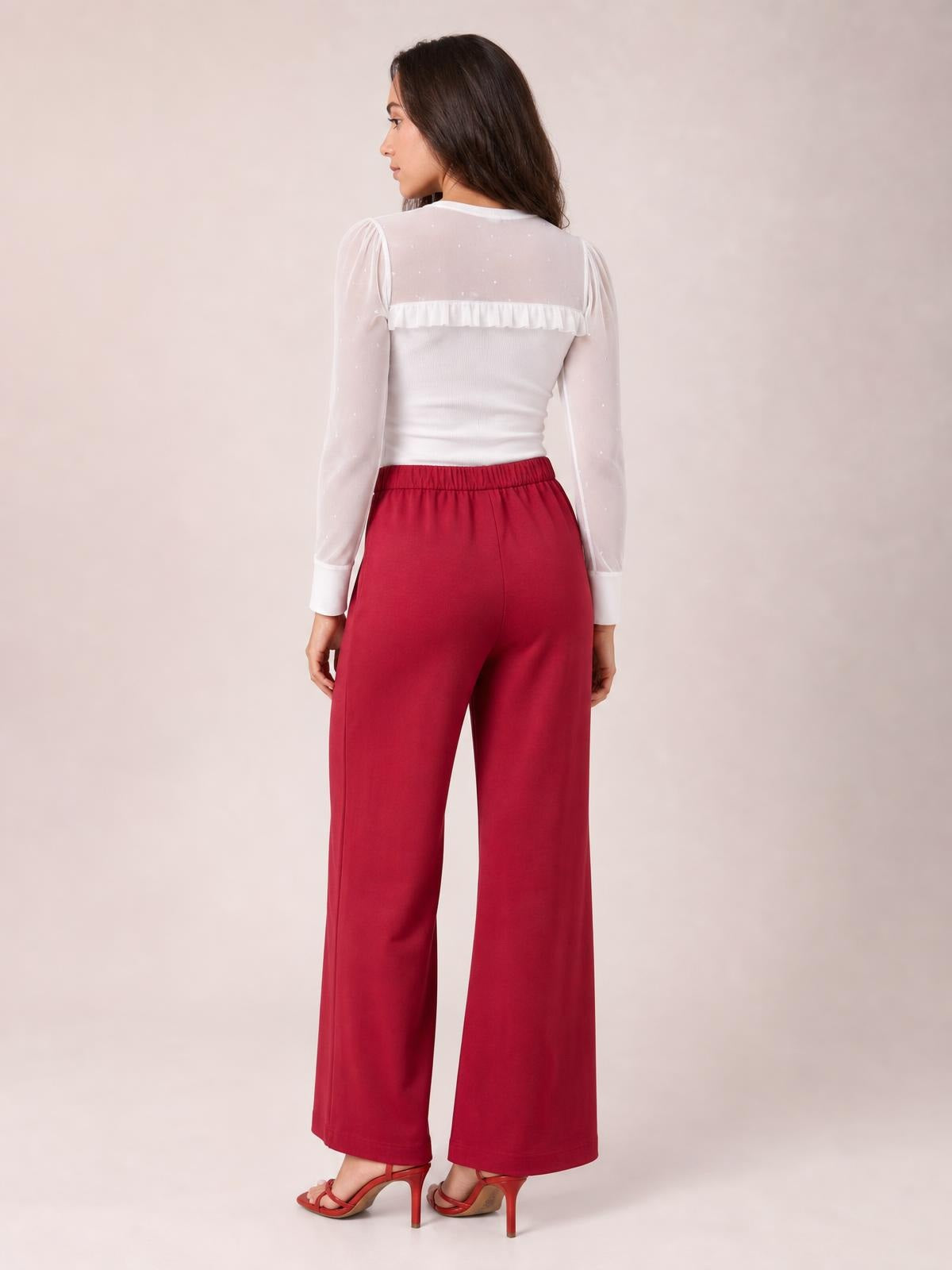 A model poses from behind wearing red high-waisted wide-leg pants with a smooth waistband and relaxed, full-length silhouette.