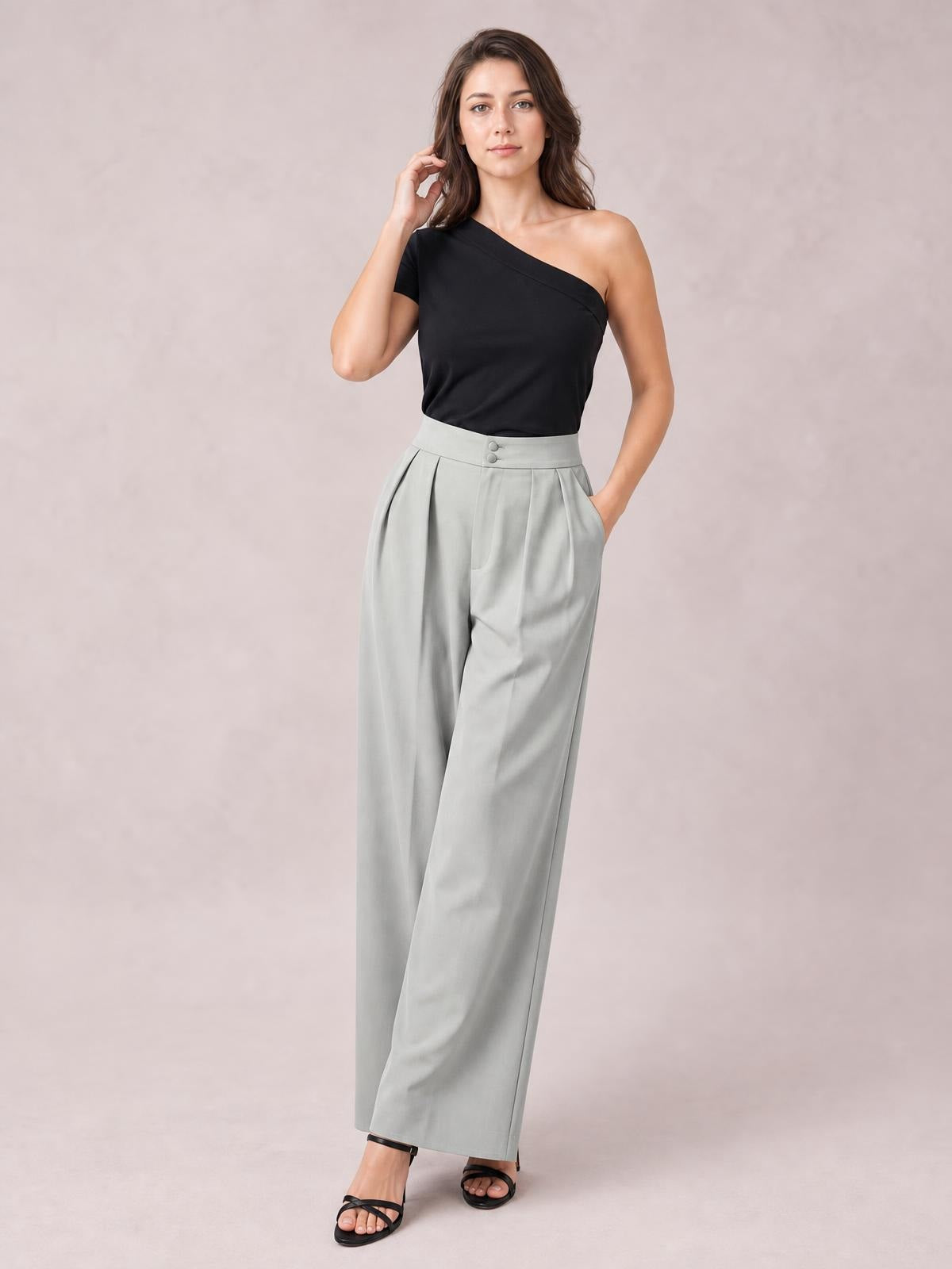 Model poses in light gray high-waisted pleated wide-leg pants with a buttoned waistband, front pockets, and a flowing full-length silhouette.
