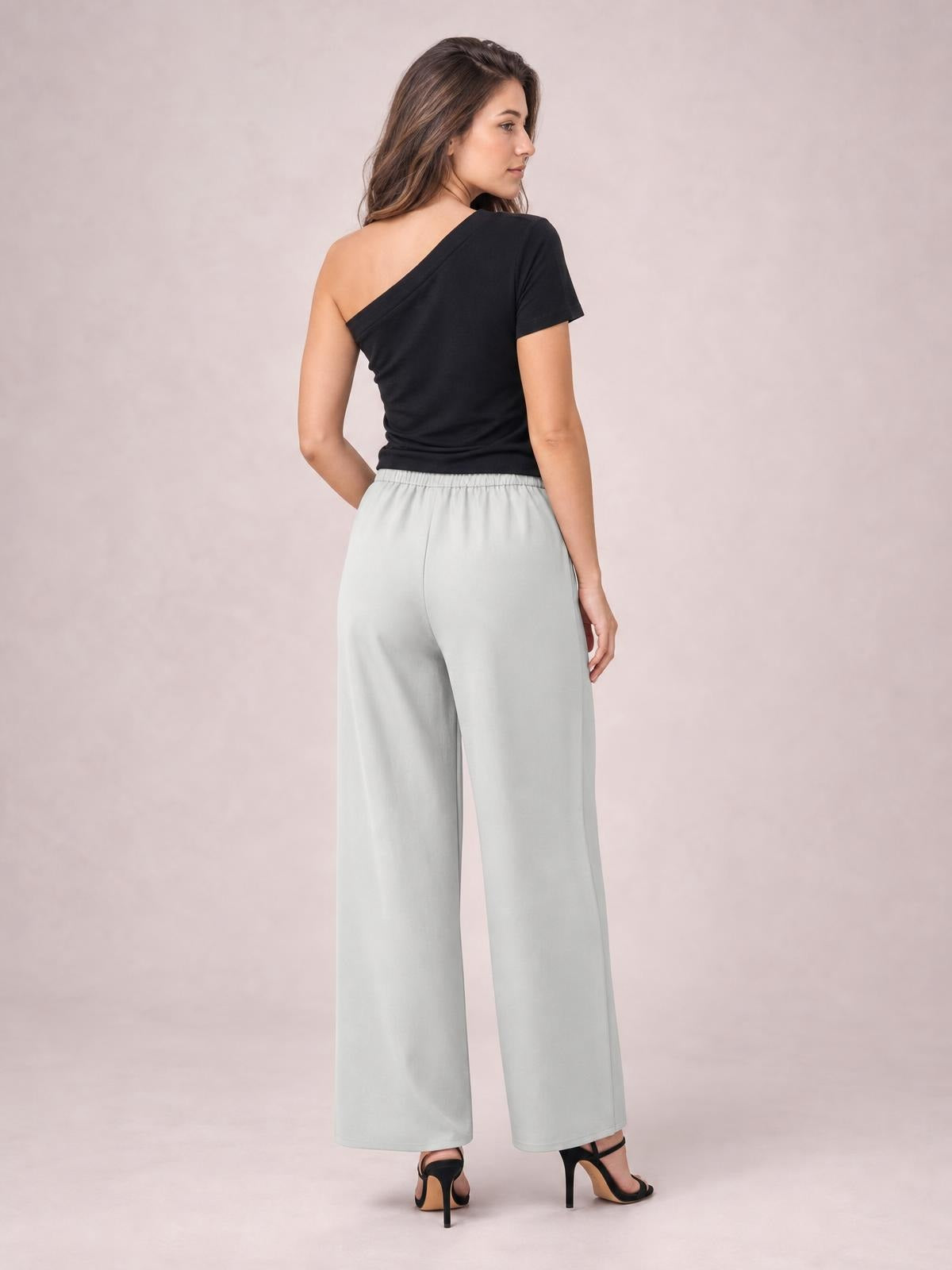 A model poses from behind in light gray high-waisted wide-leg pants with a fluid, relaxed silhouette and straight hems, paired with a black asymmetrical top.
