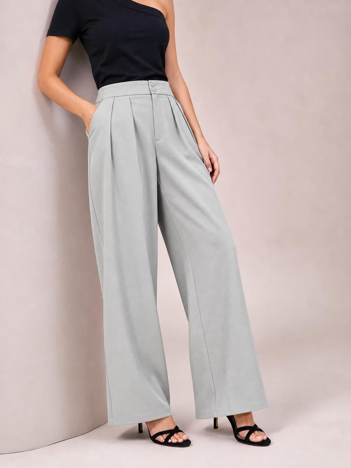 A model poses in light gray high-waisted pleated wide-leg pants with a buttoned waistband, side pockets, and a flowing full-length silhouette.
