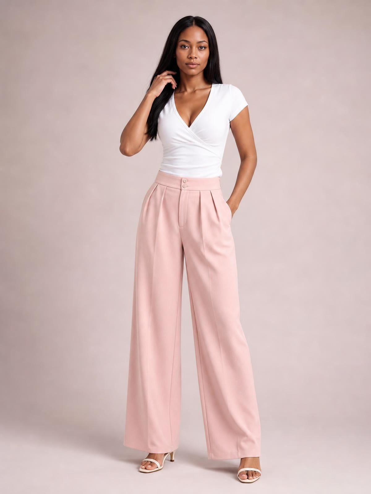 Model poses in pink high-waisted pleated wide-leg pants with a buttoned waistband, front pockets, and a relaxed full-length silhouette.