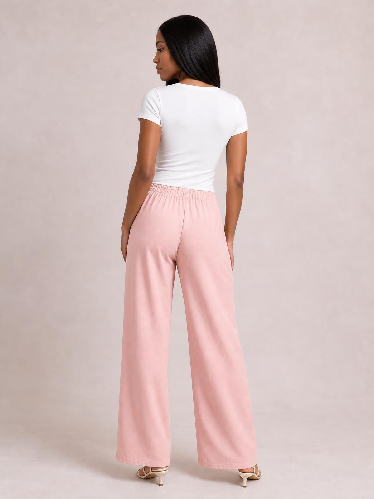 A model looks over her shoulder while wearing pink high-waisted wide-leg pants with a smooth waistband and relaxed, flowing silhouette.