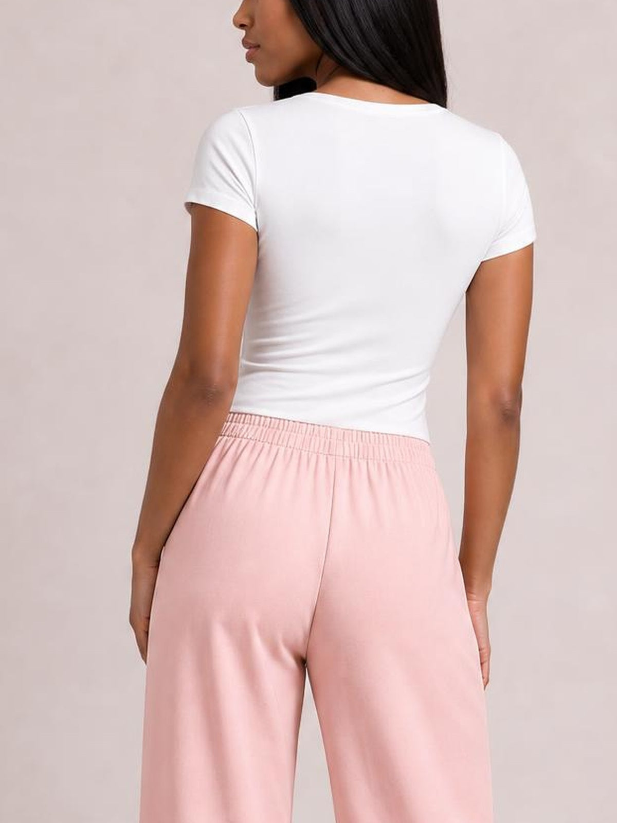 A woman stands with her hands at her sides, modeling pink high-waisted wide-leg pants with a relaxed silhouette and elasticized waistband from the back.