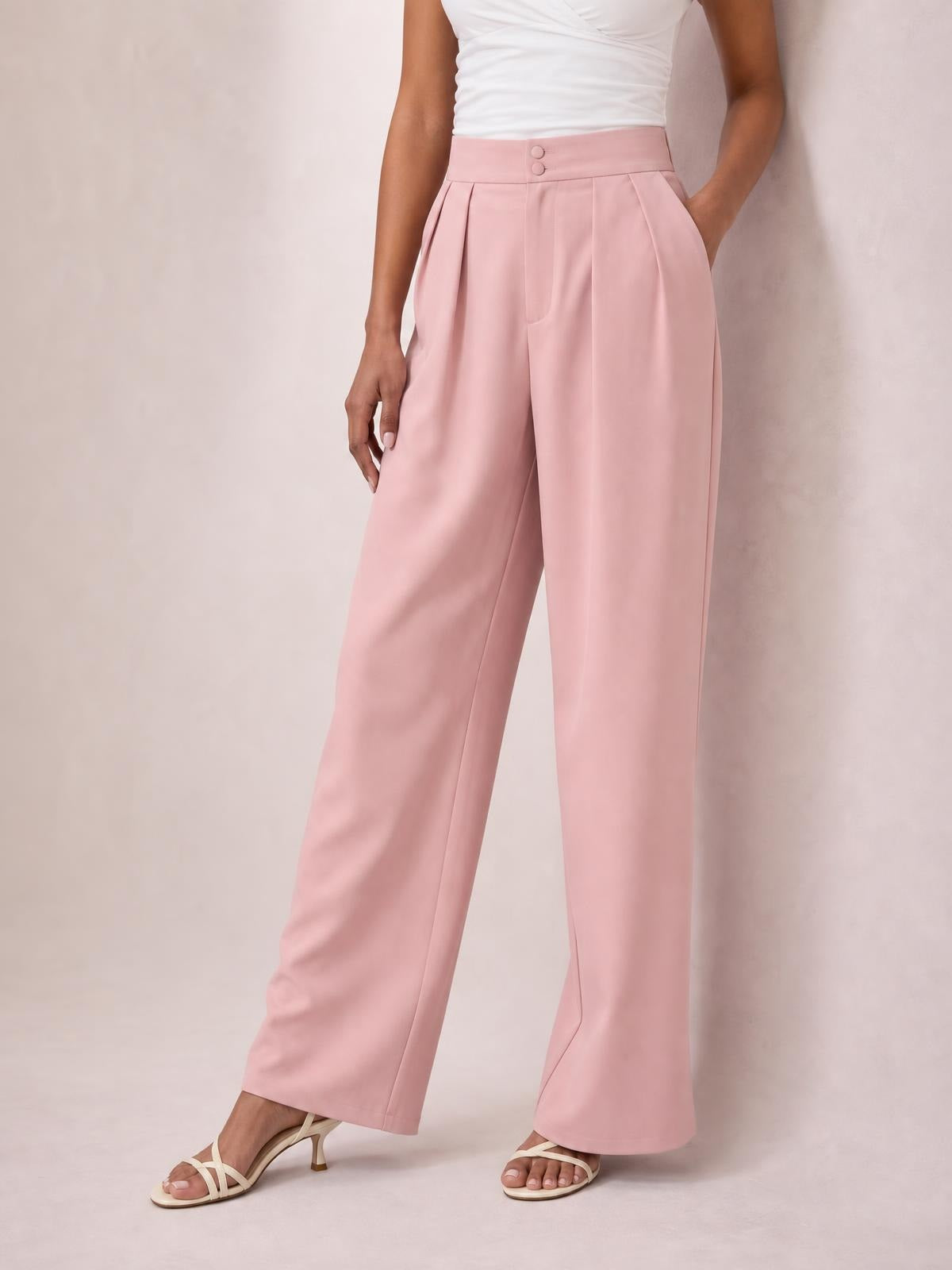 Model wearing pink high-waisted pleated wide-leg pants with a buttoned waistband, curved pockets, and a relaxed full-length silhouette.