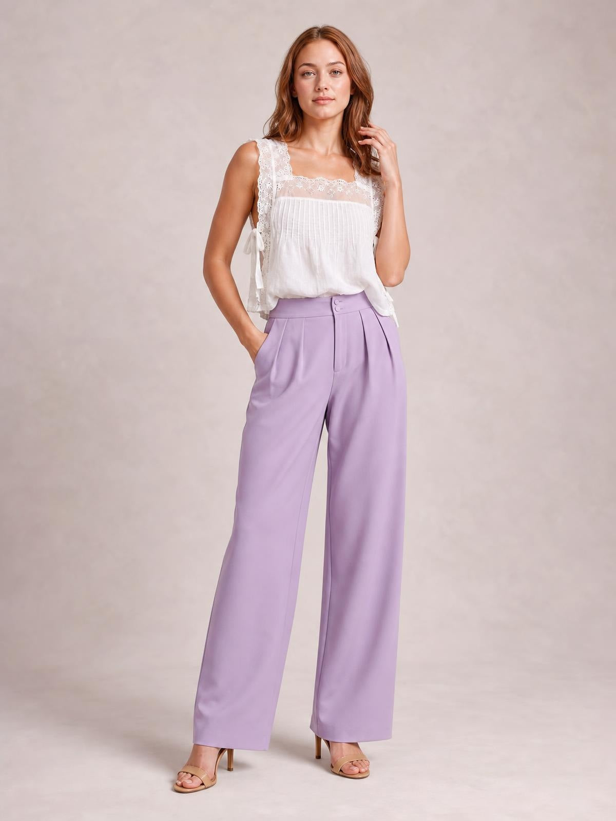 Model wearing lavender high-waisted pleated wide-leg pants with front buttons, side pockets, and a full-length relaxed silhouette.