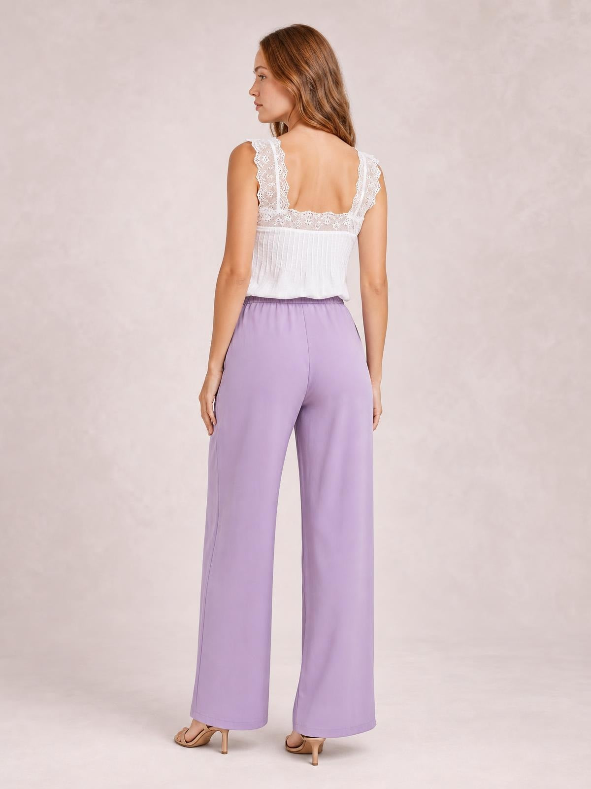 A model stands turned away wearing lavender high-waisted wide-leg pants with a smooth waistband, relaxed flowing silhouette, and full-length straight legs.