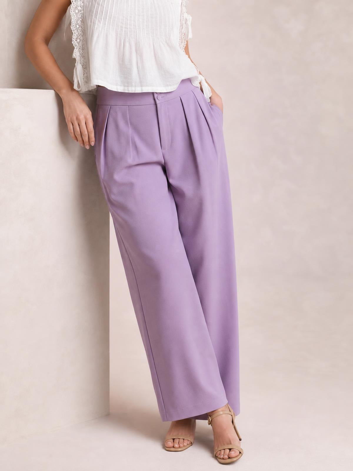 Model poses in lavender high-waisted pleated wide-leg pants with a button closure, side pockets, and a relaxed full-length silhouette.