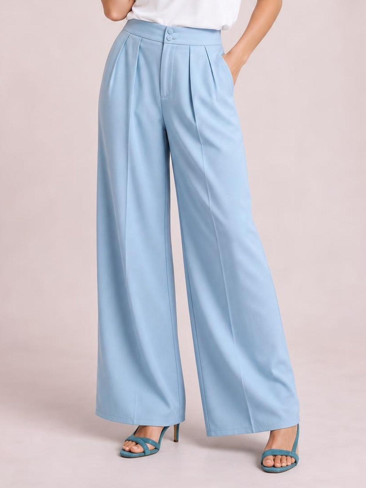 A model poses with one hand in the pocket wearing light blue high-waisted pleated wide-leg pants with a buttoned waistband and fluid silhouette.