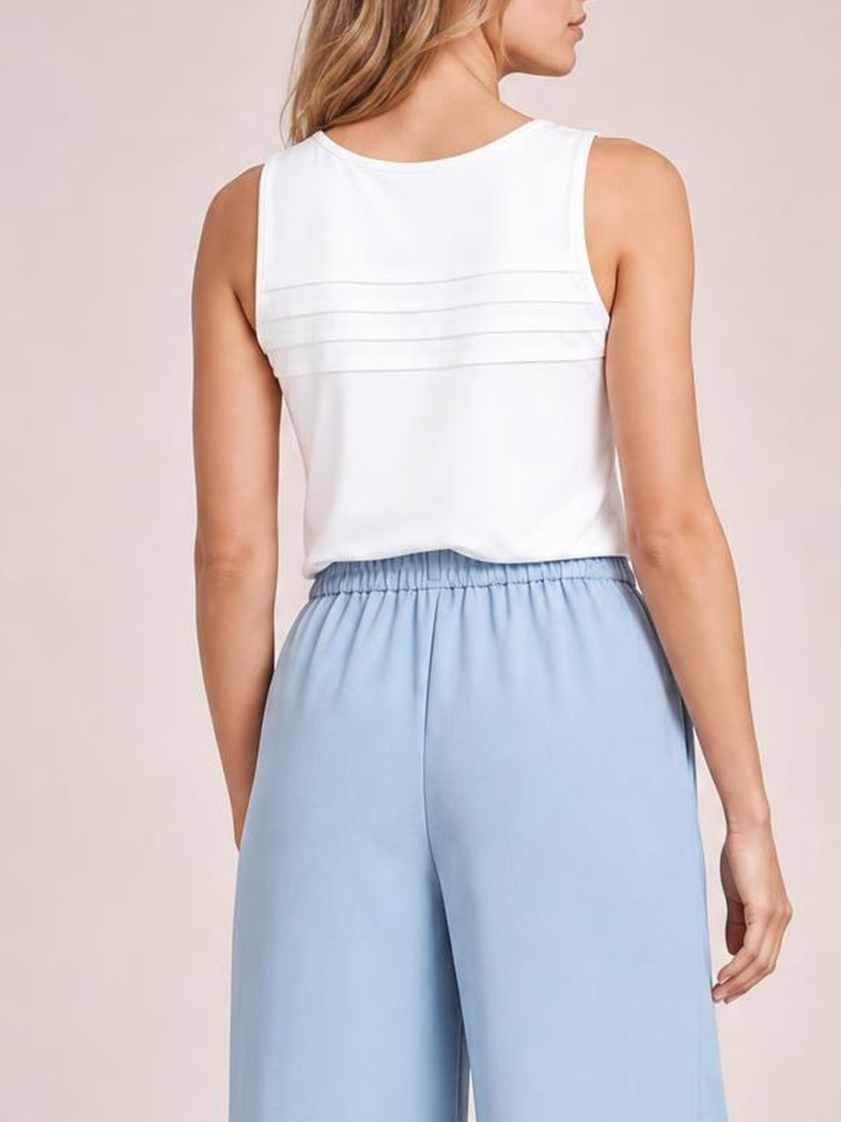 A model poses from the back wearing light blue high-waisted pleated wide-leg pants with a gathered waistband and relaxed, flowing silhouette.