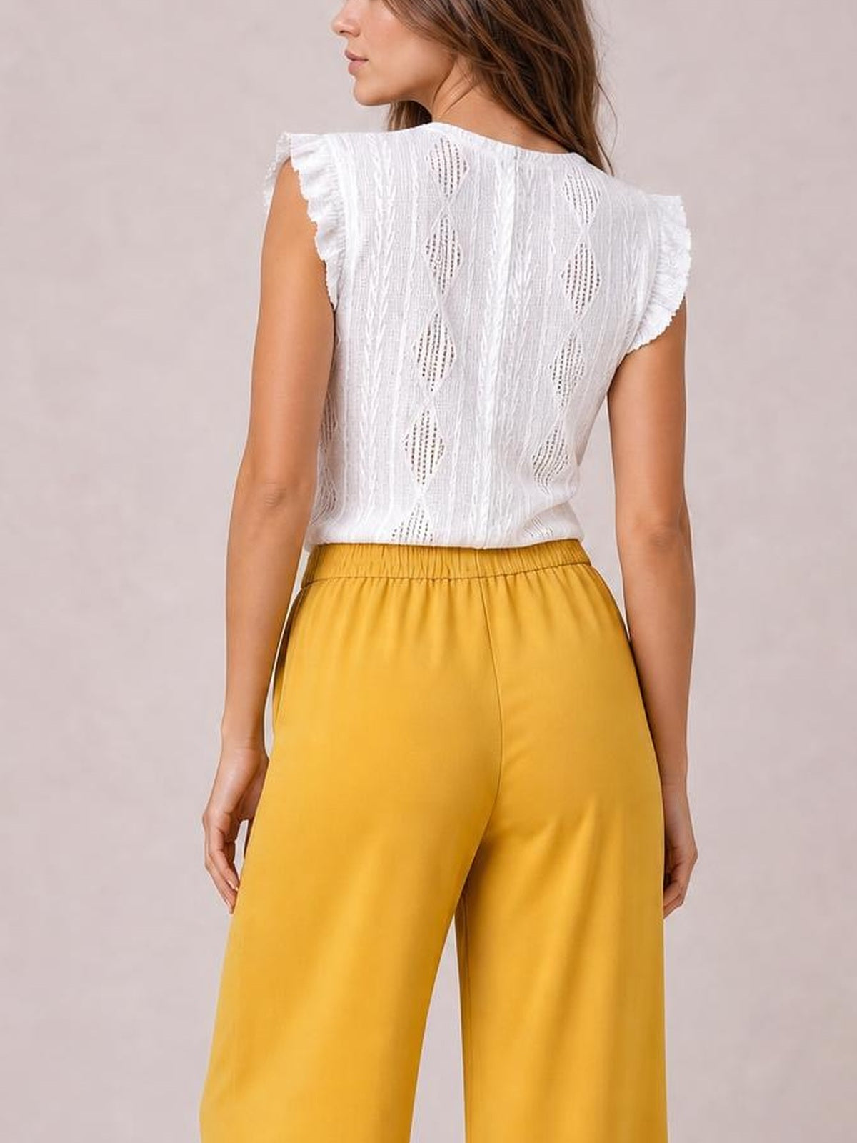 A model stands with her back to the camera wearing mustard yellow high-waisted wide-leg pants with a smooth, relaxed silhouette and gathered waistband.