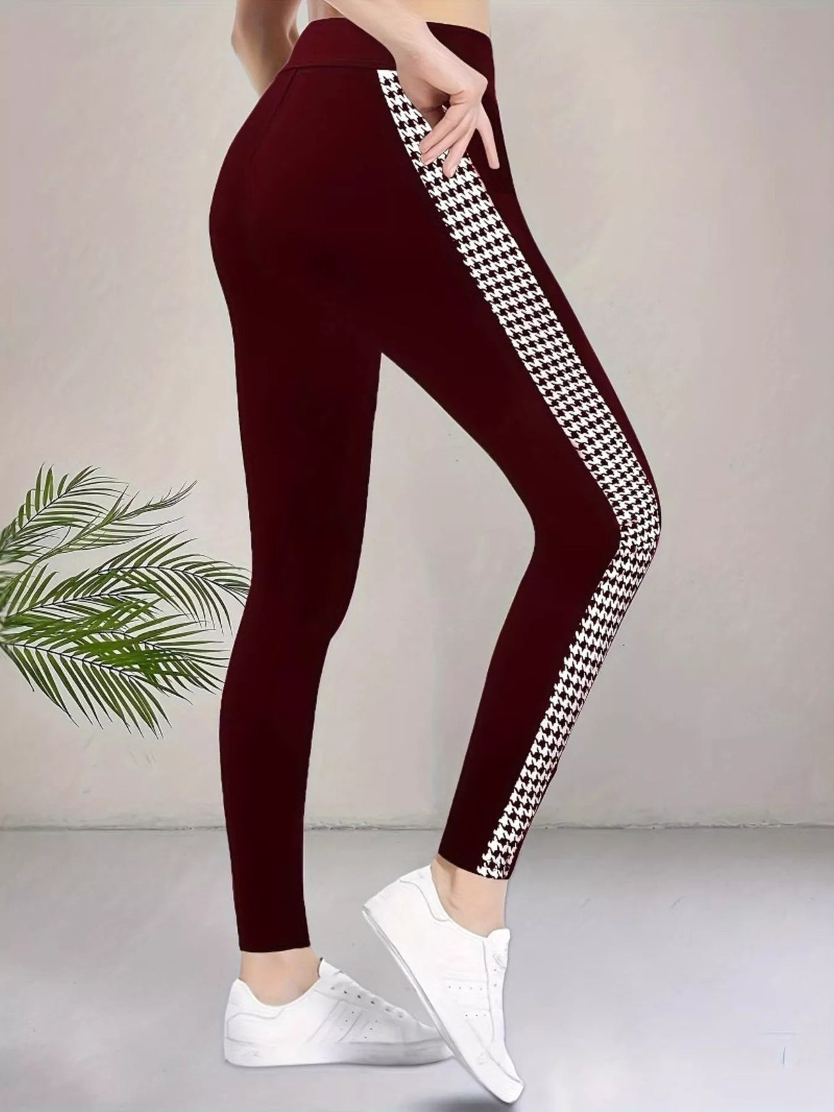 Model poses in burgundy high-waisted active leggings with a sleek fitted silhouette, visible seam detail, and contrasting side houndstooth panel.