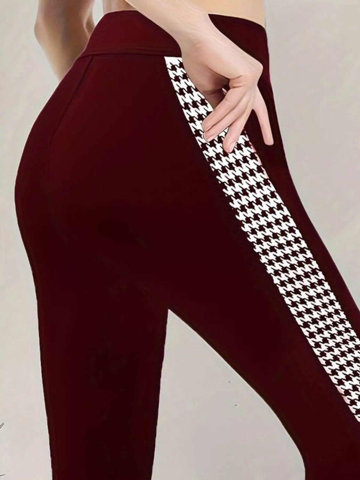 A model wears burgundy high-waisted active leggings with a fitted stretch silhouette, seam detail, and a bold black-and-white houndstooth side panel.
