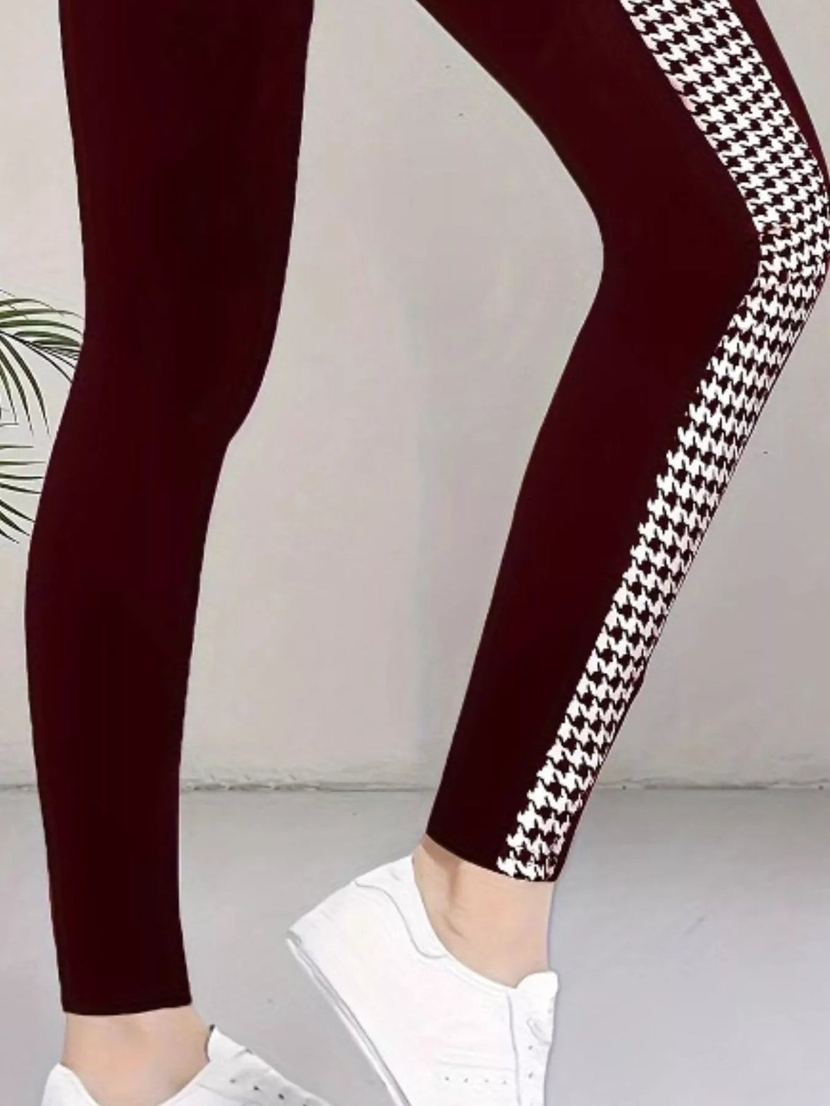 Model wears burgundy active leggings with a close, stretchy silhouette and bold white houndstooth side panels, standing with one leg crossed forward in white sneakers.