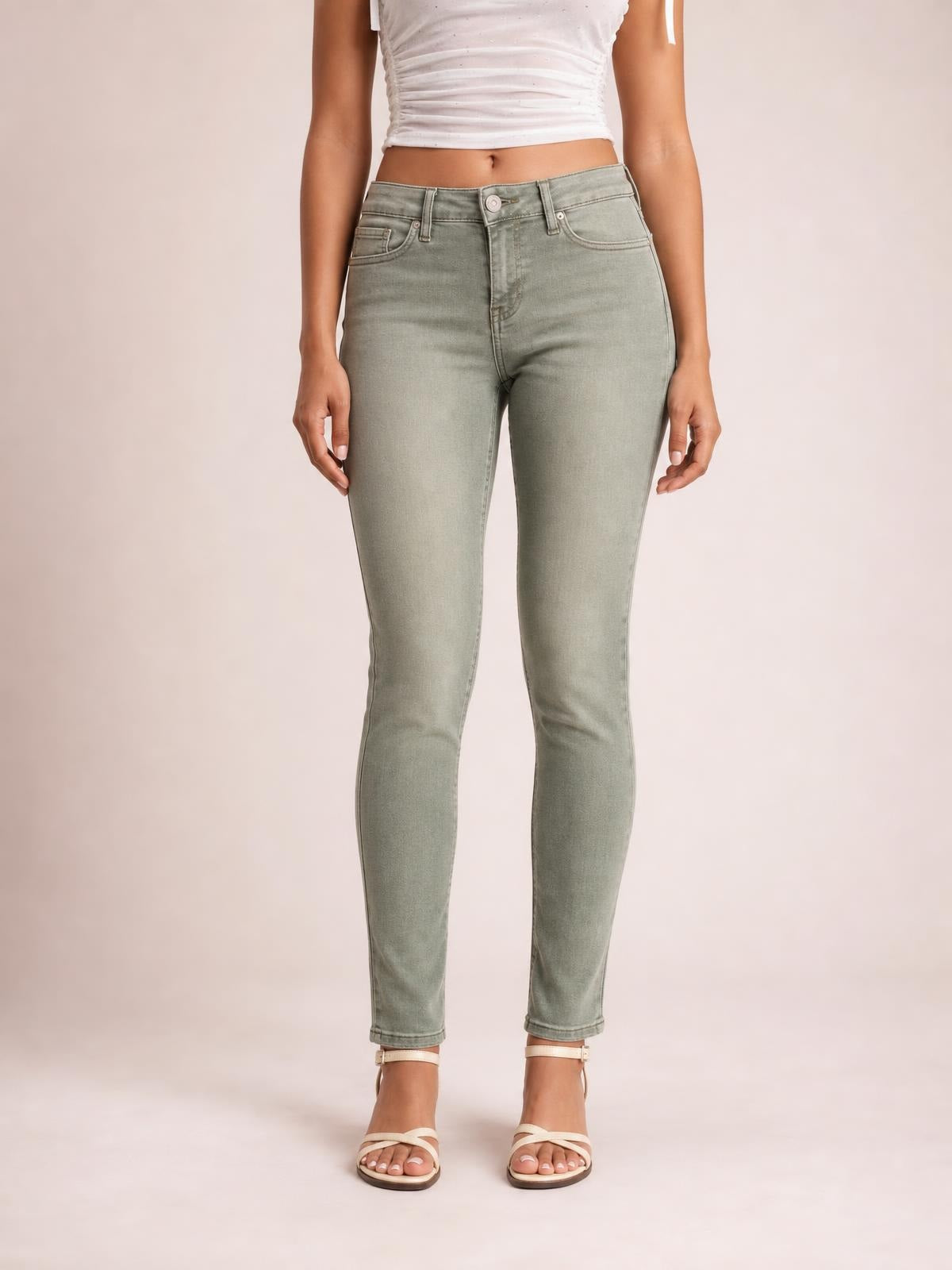A model stands facing forward in light sage high-waisted slim-fit jeans with a button closure, belt loops, front pockets, and fitted tapered legs.