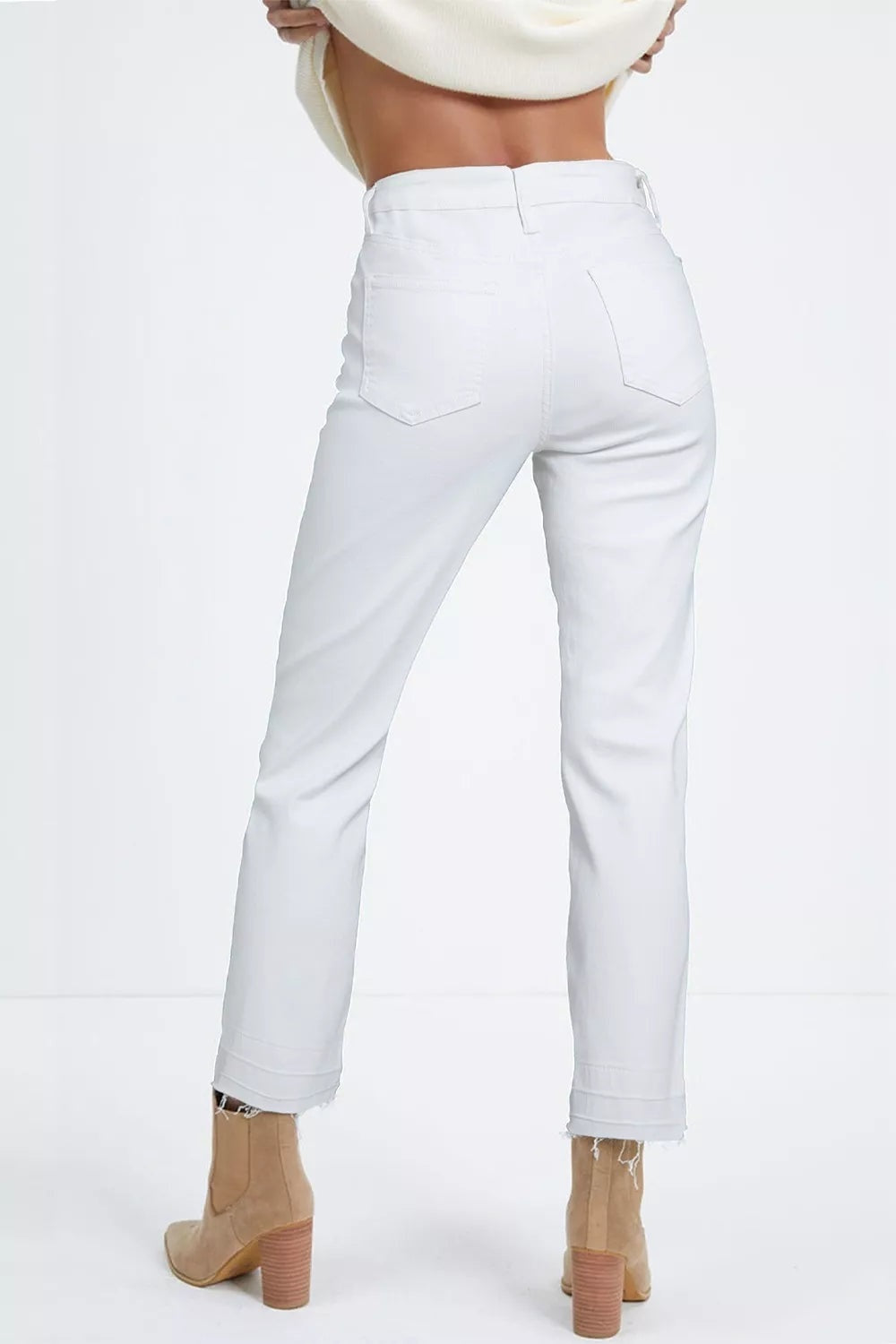 A model stands in a back view wearing white high-waisted straight leg jeans with belt loops, two back pockets, and cropped frayed hems.