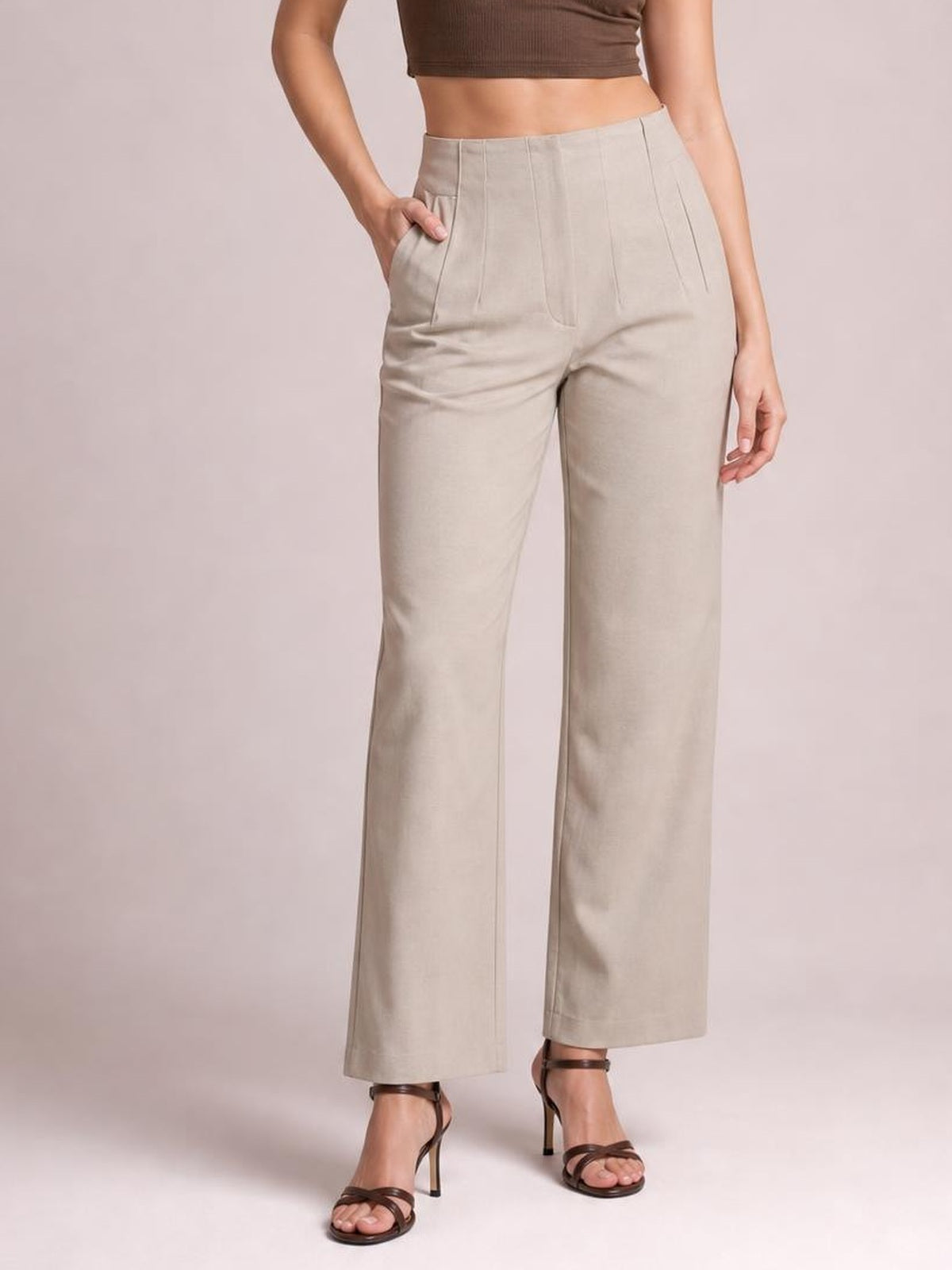 Model poses with one hand in the pocket of high-waisted beige straight-leg pants featuring front seam detailing and a tailored, ankle-length silhouette.
