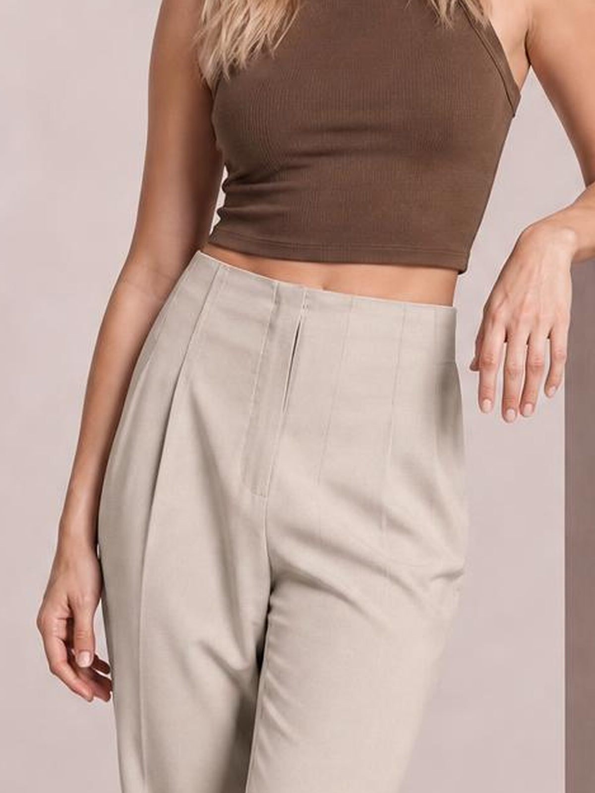 A model poses in light beige high-waisted straight-leg pants with a structured waistband, front pleats, and visible side pockets.