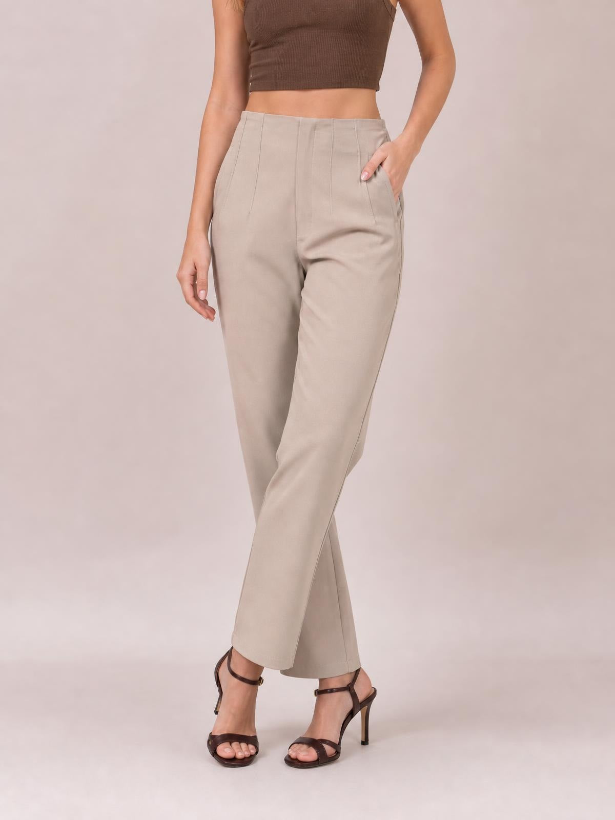A model poses in beige high-waisted straight-leg pants with visible front seam details and side pockets, one hand tucked into a pocket.