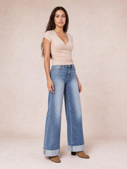 Model stands in light-wash high-waisted wide-leg jeans with front pockets, contrast stitching, and wide rolled cuffs.