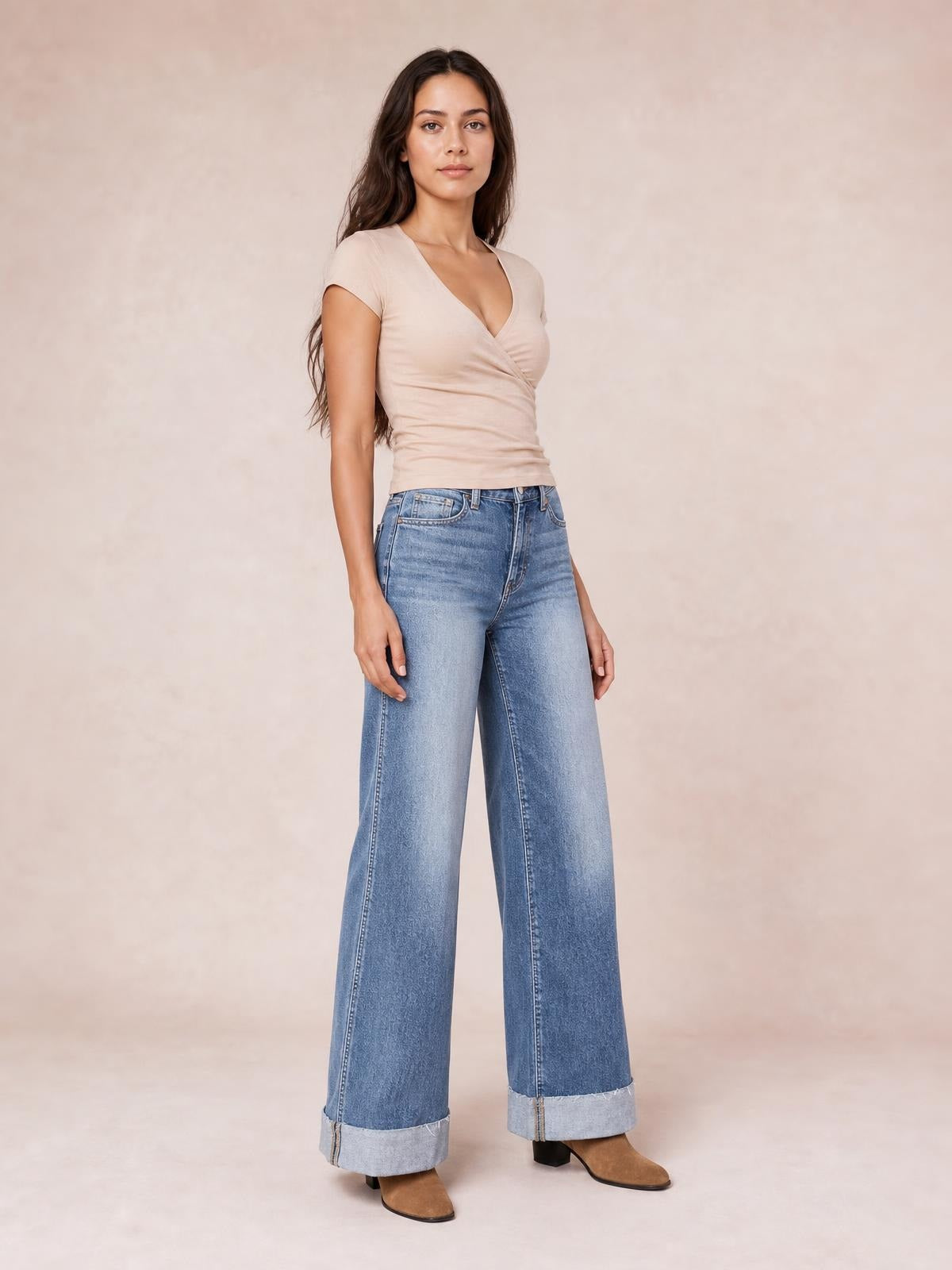 Model stands in light-wash high-waisted wide-leg jeans with front pockets, contrast stitching, and wide rolled cuffs.