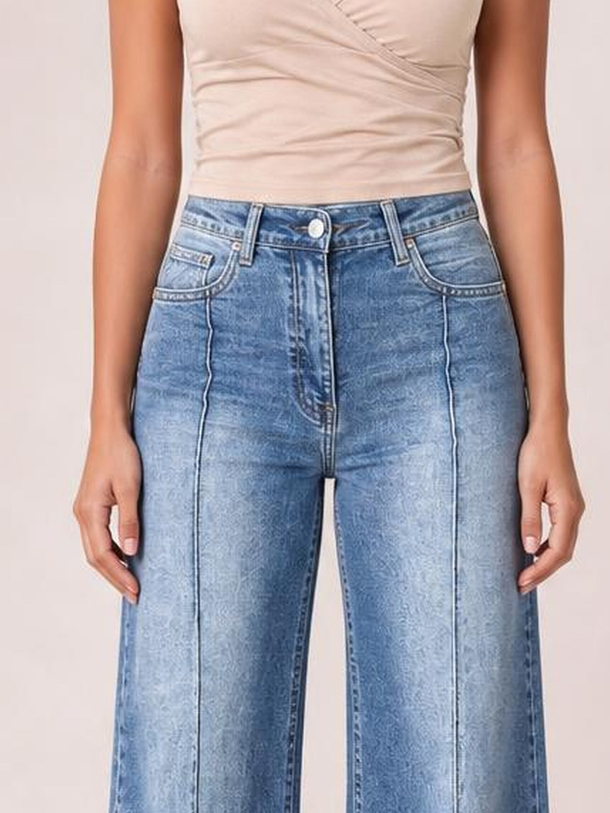 A model poses with hands at her thighs, wearing light blue high-waisted wide-leg jeans with contrast stitching, belt loops, a button fly, and front pockets.