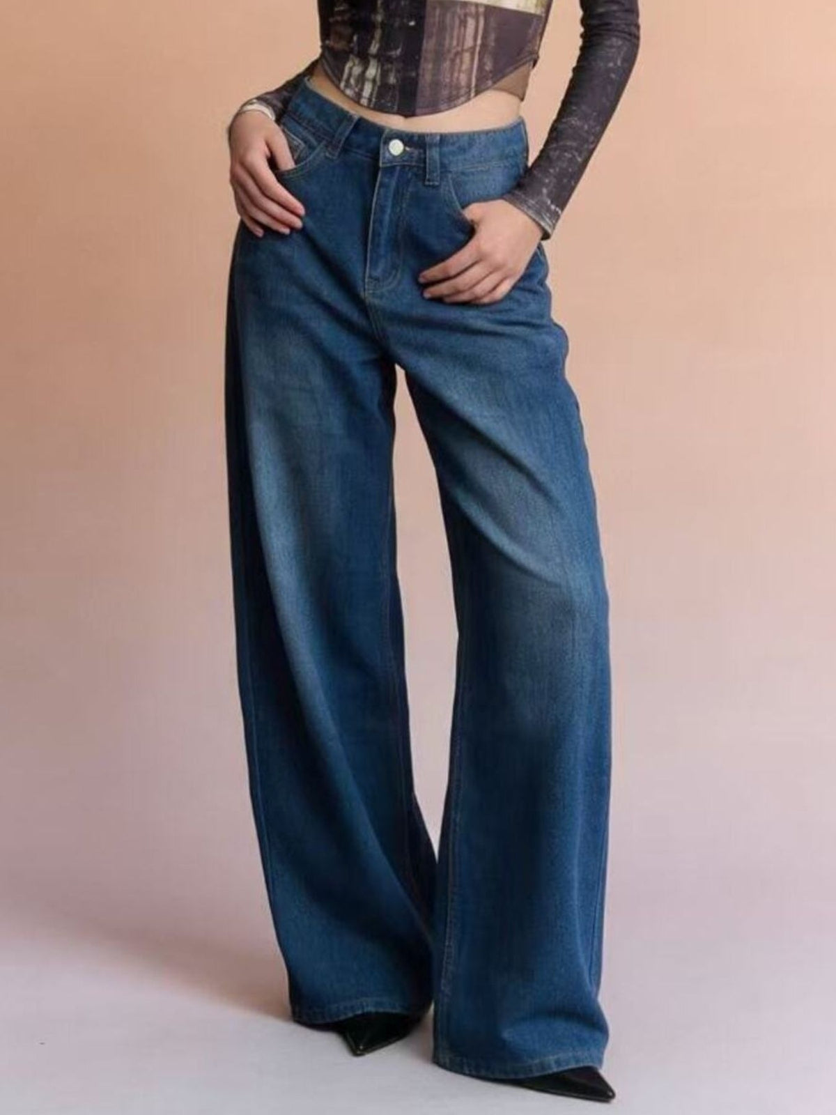 Model poses with hands at the hips in dark blue high-waisted wide leg jeans featuring a button fly, belt loops, pockets, and a fluid full-length silhouette.