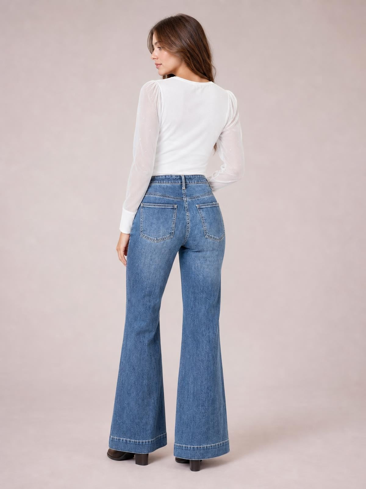 A model looks over her shoulder in washed blue high-waisted wide leg jeans with back patch pockets, belt loops, structured seams, and wide cuffed hems.