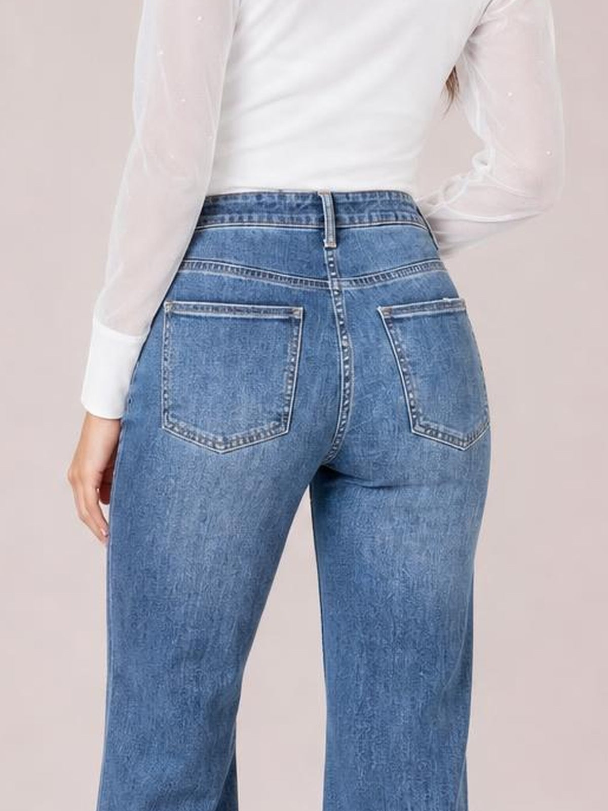 Model shown from behind in washed blue high-waisted wide-leg jeans with a structured waistband, zipper fly, contrast stitching, and two back patch pockets.