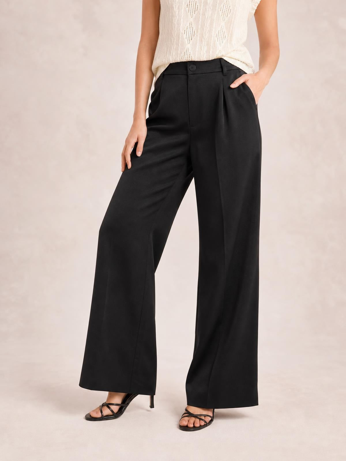 Model wearing black high-waisted wide-leg pants with a buttoned waistband, belt loops, side pockets, and a fluid full-length silhouette.