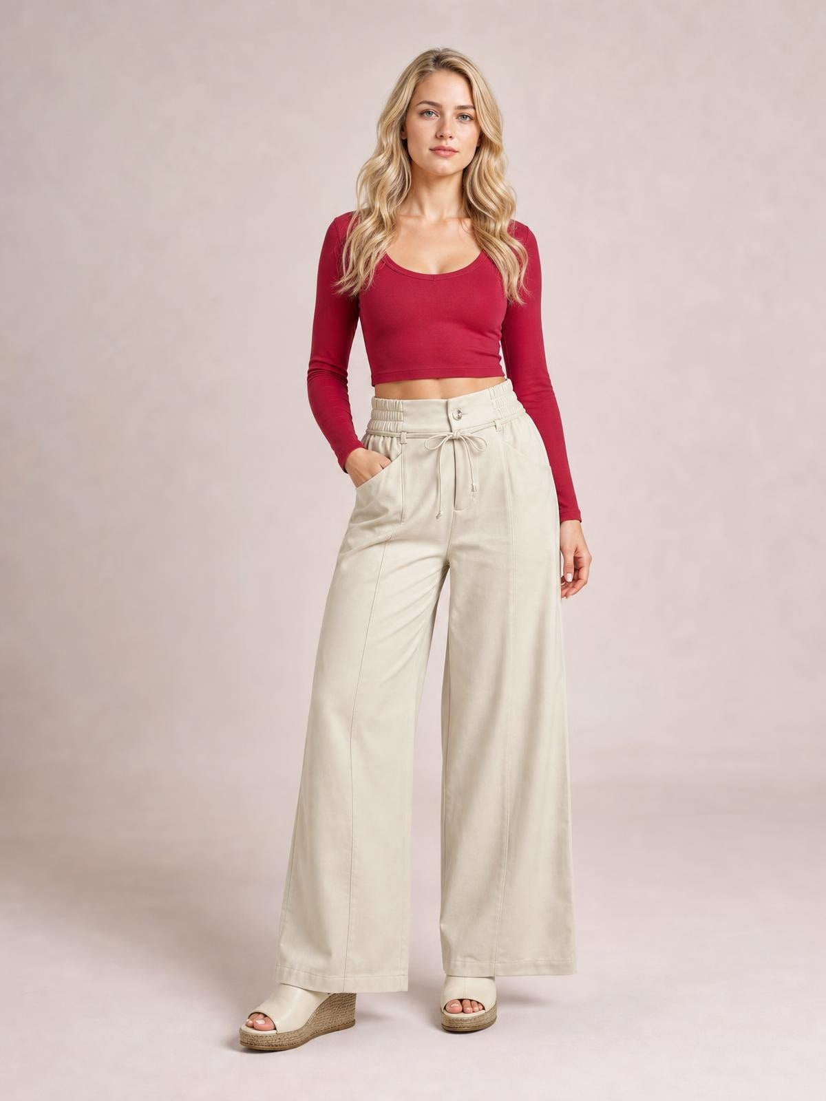 Model wearing cream high-waisted wide-leg pants with a buttoned, tied waistband, front pockets, and long relaxed legs.