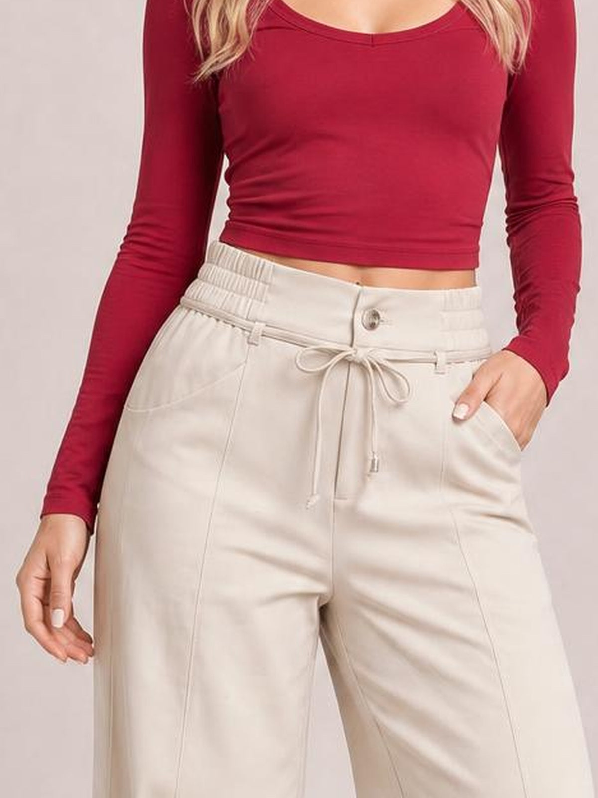 Model poses in cream high-waisted wide-leg pants with a button closure, tied drawstring waist, and spacious front pockets.